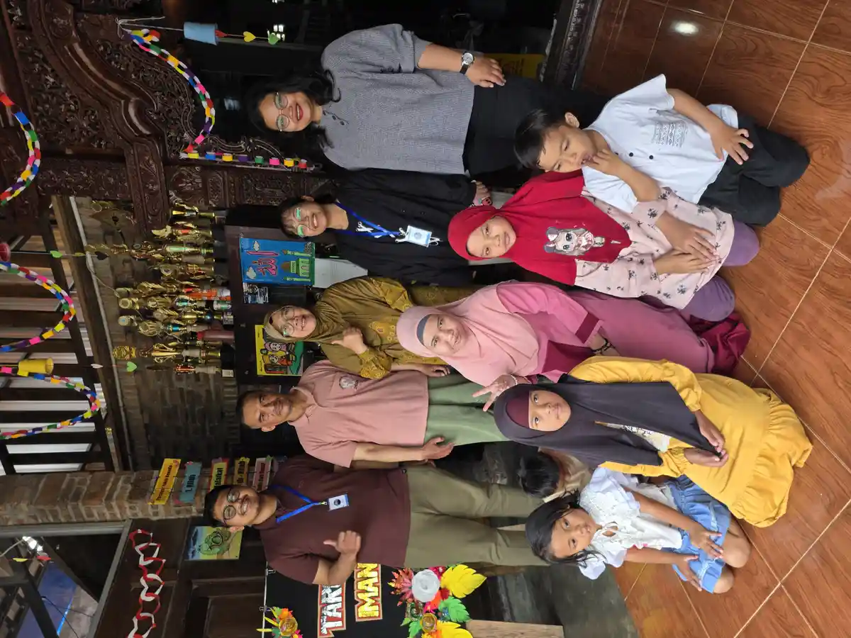 Keluarga berfoto bersama di depan rumah tradisional, menggambarkan pentingnya dukungan keluarga bagi penyandang disabilitas