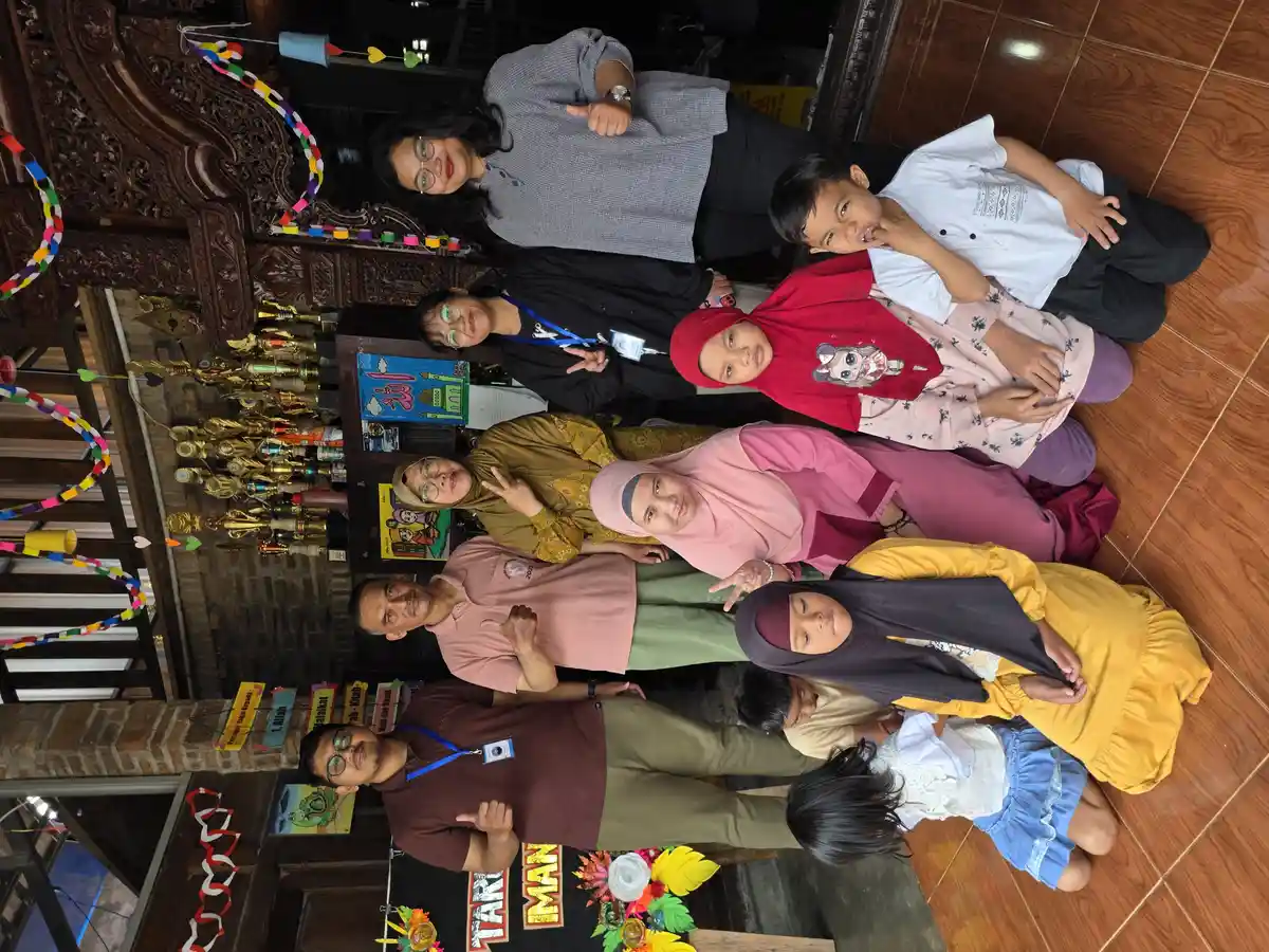 Keluarga berfoto bersama di depan rumah tradisional, menggambarkan keharmonisan dan dukungan keluarga dalam mendampingi penyandang disabilitas