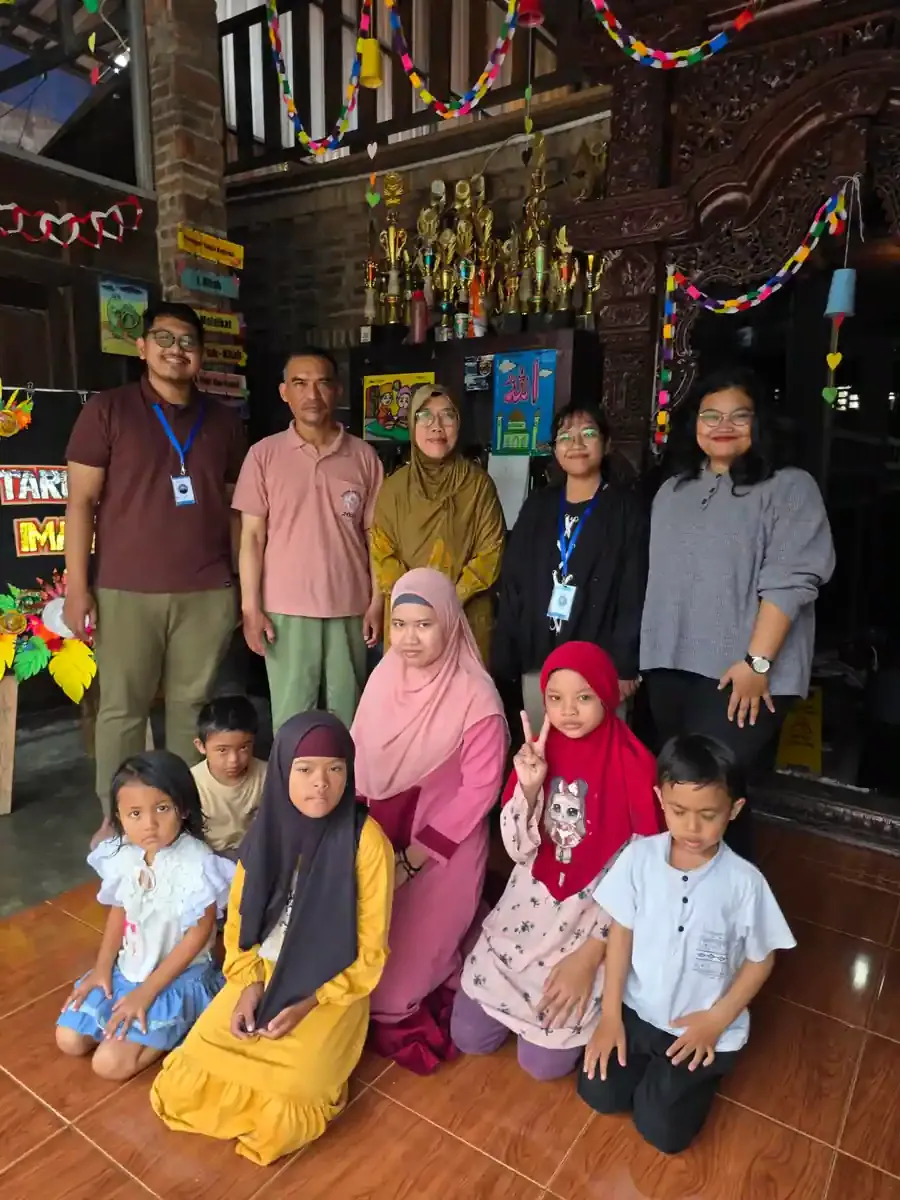 Guru, tamu, dan beberapa siswa berfoto bersama di ruang sekolah berhias pita warna-warni dan rak piala