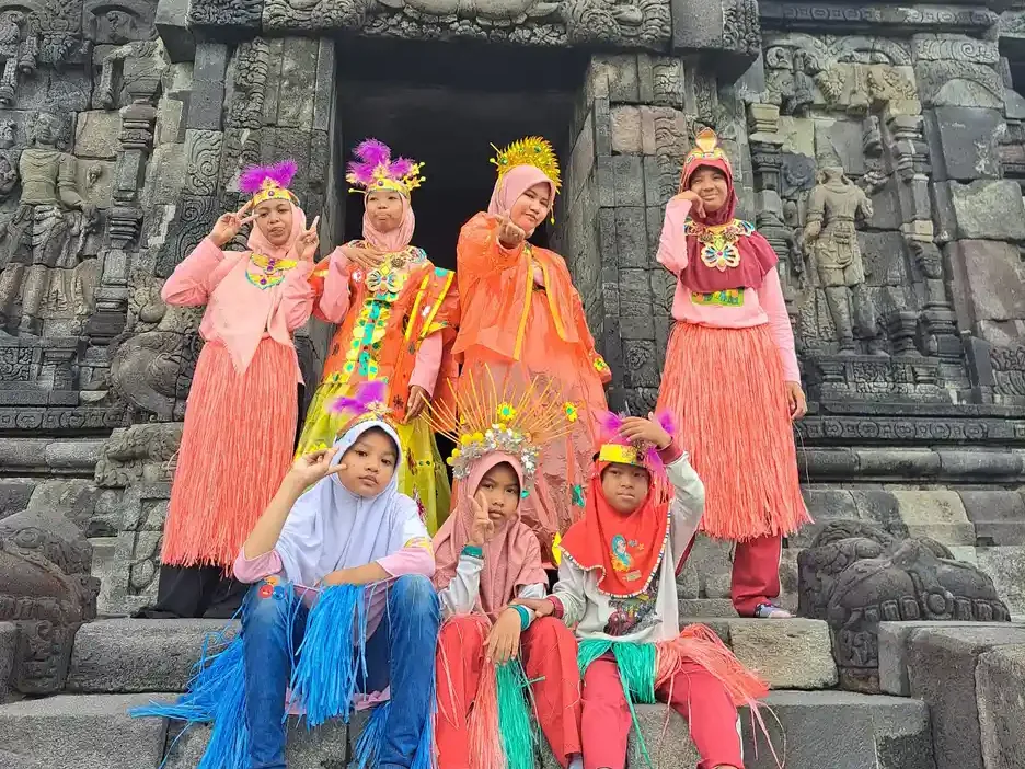 Rombongan anak dan pendamping berkostum tari tradisional warna-warni berpose ceria di tangga batu sebuah candi