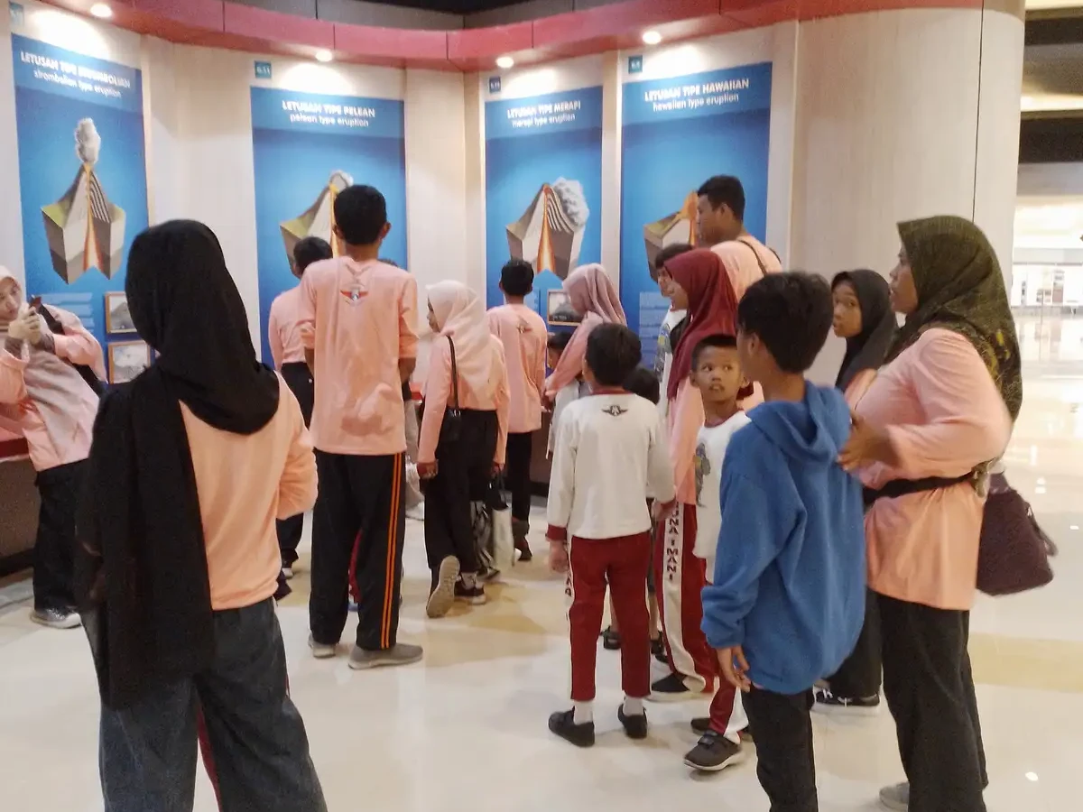 Anak-anak dan pendamping berdiri bersama di ruang pamer museum dengan panel informasi di belakang mereka