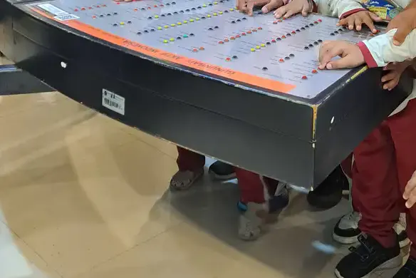 Beberapa tangan anak menyentuh papan permainan interaktif di museum, sebagian anak berdiri berdampingan di sekeliling meja