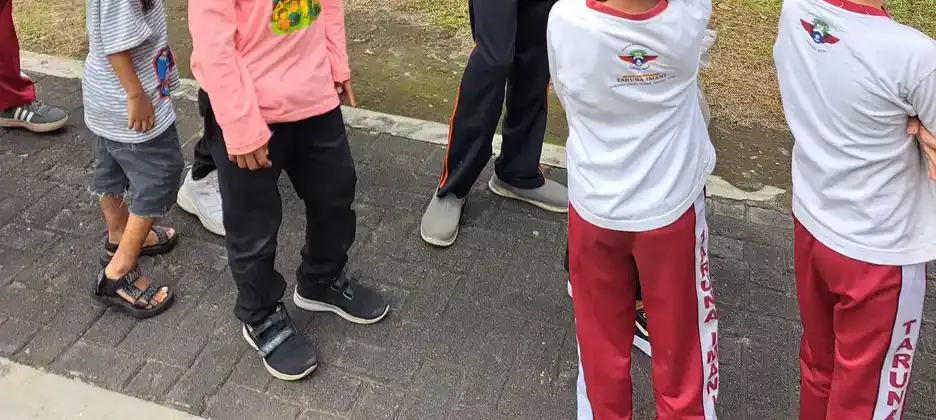 Kaki beberapa anak bersepatu dan bersandal berdiri dan melangkah di jalur paving taman